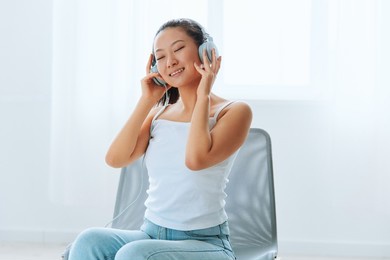 relaxing dancing cheerful tanned lovely young asian woman in headphones moves to music at home interior living room. sound studio stream, social media concept. cool offer banner wide angle