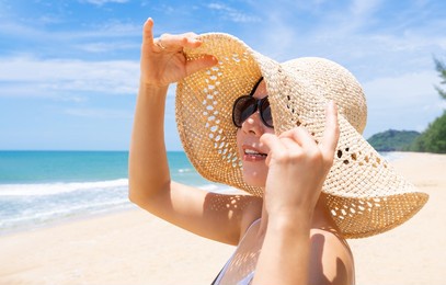 portrait of stylish asian woman in swimsuit on beautiful tropical beach with straw hat, sunglasses to protect sunlight. blue sky, eyes protection, sunscreen, sunny, skin, copy space, relax, holidays.