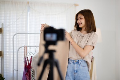 young asian seller girl showing woman clothes and making video live streaming online at home. online market with social media concept.