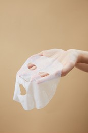 front view of hand holding a mask in beige background for cosmetic advertising 