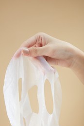 front view of hand holding a mask in beige background for cosmetic advertising 