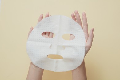 front view of hand holding a mask in beige background for cosmetic advertising 