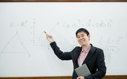 an asian male teacher in a classroom near the whiteboard is writing and teaching a lesson with a special lecture in a class column. math teacher explains arithmetic sums to university students.
