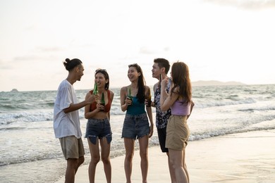 group of asian young man and woman having party on the beach together. attractive friends singing and dancing while walking and running at seaside enjoy holiday vacation trip in tropical sea island.
