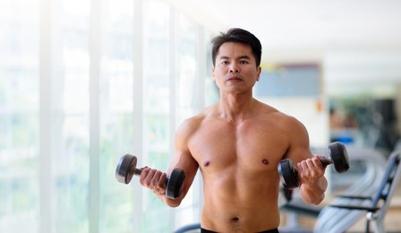 man exercising in gym. asian bodybuilder lifting weights. sport and healthy activity for young male. active chinese athlete in training. body building exercise work out.