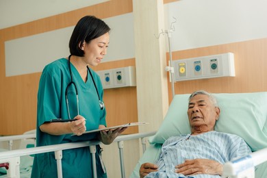 hospitalized man lying in bed while doctor checking his pulse. doctor or nurse examining senior male patient in hospital room.