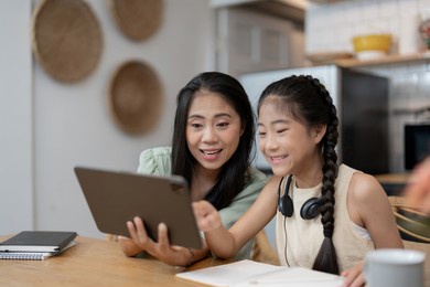 portrait of cheerful asian mother and daughter using digital tablet in kitchen at home