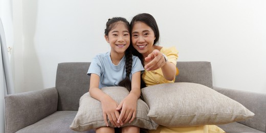 excited young asian mother and little girl watching television programs. lifestyle and spends leisure at home.