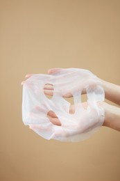front view of hand holding a mask in beige background for cosmetic advertising