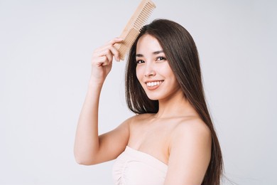 beauty portrait of happy smiling asian woman with dark long hair combing wooden comb on white background isolated