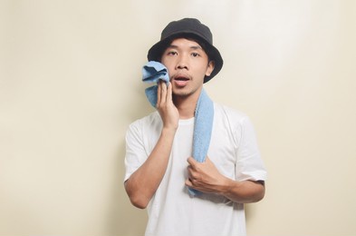 asian man wearing bright white t-shirt with black hat wiping sweat on isolated background