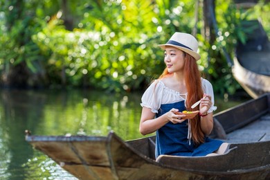 young asian woman tourist is travel with wooden boat in floating market in thailand and having local street food for southeast asia tourism