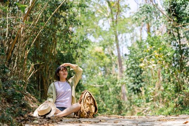 cute young woman taking a break from forest walk in green tree background with straw fog, backpack