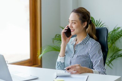 smiling young asian woman talking on the phone and working at home.