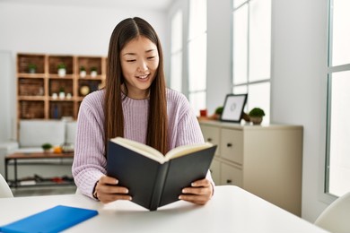 young chinese girl reading book sitting on the table at home.