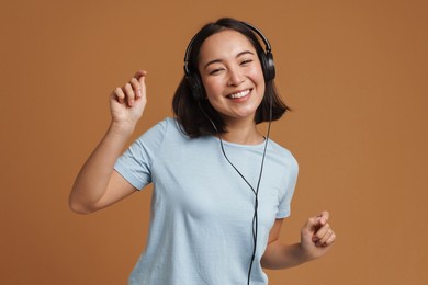 young asian woman in headphones dancing while listening music isolated over beige background