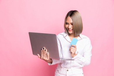 portrait of beautiful asian woman holding credit card and laptop on isolated background, portrait concept used for advertisement and signage, isolated over pink background.