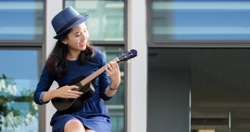 asian girl practice playing ukulele string instrument and singing in bright day. ukulele is string music instrument easier play and soft sound good for pop music.