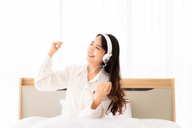 beautiful young asian woman in headphones listening to music and dancing on bed at bedroom in morning time