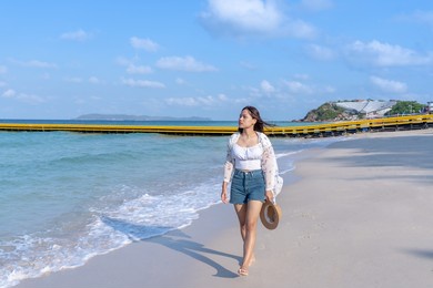 asian woman holding a straw hat walking on the beach looking at the blue sea travel lifestyle during summer vacation in thailand.