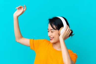 young vietnamese woman isolated on blue background listening music and dancing