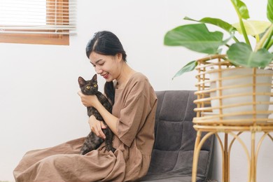 pet lover concept, young asian woman sitting to relax on sofa on floor to playing and hugging cat.