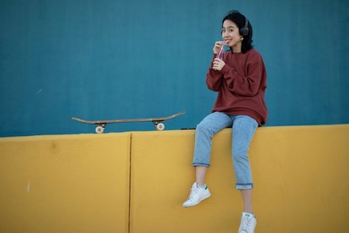 beautiful young woman with skateboard. urban chinese girl sitting outdoors, listening the music