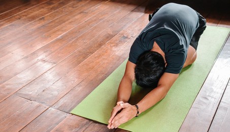 sporty asian man in black is doing yoga while exercising on yoga mat at home with wooden floor.man yoga practice pose training healthy living concept