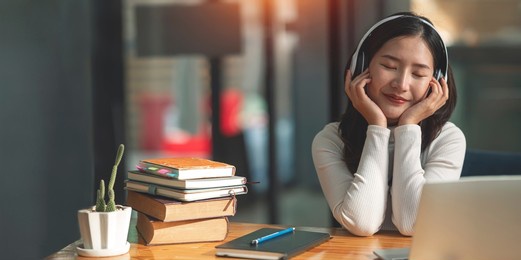 female asian college student wearing headphones enjoys online music.