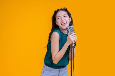 ready to party cheerful asian female woman signing joy fun toothy smile big laugh wearing casual cloth freshness action pose pretending perform in concert studio shot on yellow background
