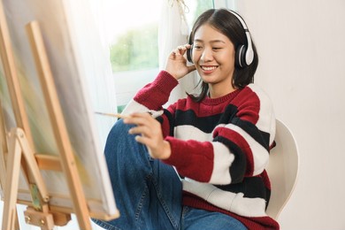 the art concept, asian female artist with headphone listening music and painting artwork on canvas.
