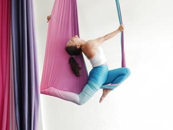 mature woman pose in hammock performing aerial yoga or flying yoga exercise against white wall background in yoga studio room. healthy lifestyles and emotional health of middle aged people concepts.