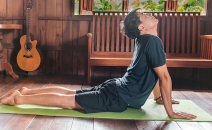 sporty asian man in black is doing yoga while exercising on yoga mat at home with wooden floor.man yoga practice pose training healthy living concept