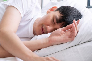 tired asian handsome man sleeping peaceful on white pillow comfortable in morning at apartment white background. casual asian young male asleep cozy good dream in bedroom. lifestyle relax concept