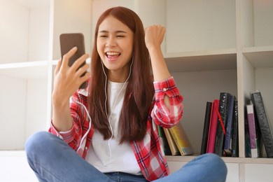 happy teens asian female college student receiving an unexpected email or good news from her university via smart mobile phone.