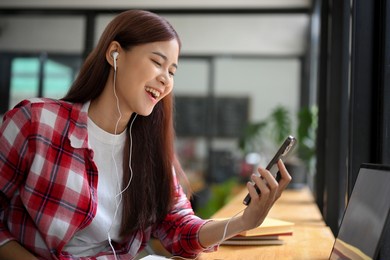 attractive and charming young asian woman enjoy listening to music on smartphone, wearing an earphones and chilling in the cafe.