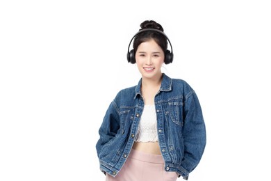beautiful young asian woman wearing jeans joyful listening to music on headphones isolated on white background studio portrait.