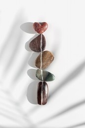 top view still life sea stones, pebbles united by one vertical row with heart stone above with palm leaf shadow. natural rocks natural tones. summer minimal style flat lay, love and romance concept 