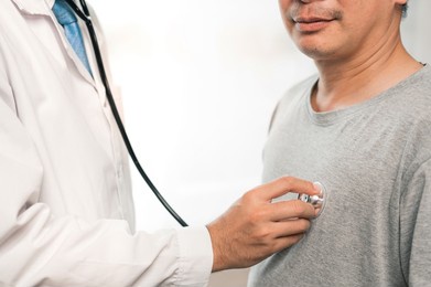 health care and people concept - doctor with stethoscope  and checking heartbeat for young asian man in hospital.