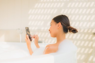 portrait young asian woman using smart mobile phone in bathtub for spa concept