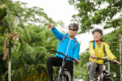 positive asian couple enjoying bicycle ride in city park