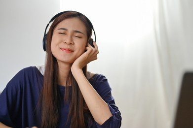 cheerful millennial asian female with modern wireless headphones listening to music in her workspace.