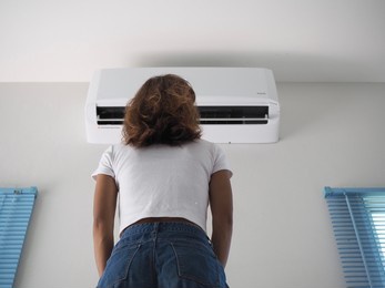 woman reaching for air conditioning in background 