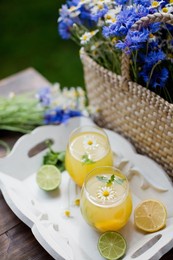 glasses with lemonade with mint, lime, lemons and orange on a white wooden tray near straw bag with wildflowers. summer drinks concept