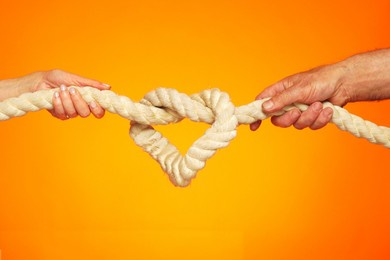 image of a heart in the form of a rope knot. male and female hands hold on to a thick rope. knot tightening. the concept of strong love and inextricable relationship.                                