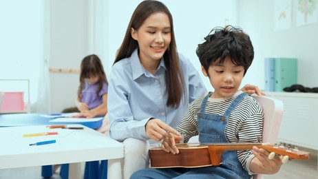 young asian teacher teaching guitar and ukulele to his little boy.little boy learning guitar at kindergarten.close up,ukulele class at school. child learning guitar from her teacher.musical education.
