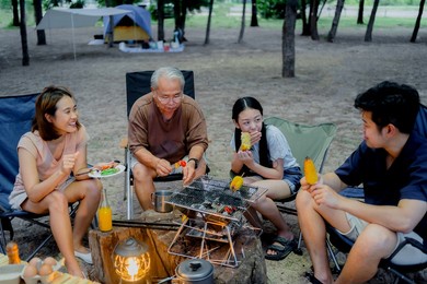 happy asian family having barbecue together. cooking grilled bbq for dinner during camping on summer beach.
