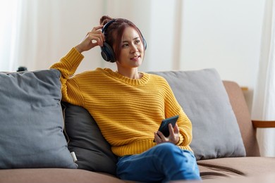 portrait of asian woman sitting at sofa and listening to music on phone at home by phone.