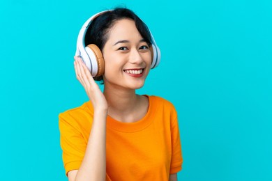 young vietnamese woman isolated on blue background listening music