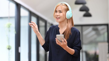 pretty asian woman wearing headphones enjoy favorite song while spending free time at home. mood, hobby, modern wireless technology concept